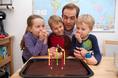 The kids patiently wait for their aging father to quit talking so they can blow out the candles and eat some cake already